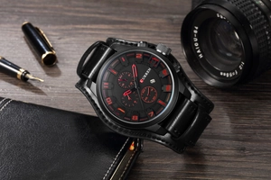 Macro shot of black dial chronograph with red numerals on a dark wooden surface