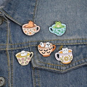 Set of 5 cute cartoon enamel pins with animals in tea cups on a blue denim jacket background