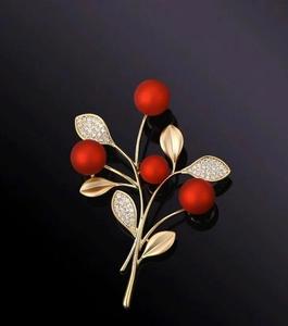 Dettaglio della spilla a ramo di bacche dorate con perle rosse e foglie di cristallo