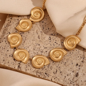 Detail of 18K gold plated NK chain necklace with matte shell charms on a stone texture