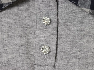 Close-up of grey knit fabric with floral rhinestone buttons and plaid collar detail