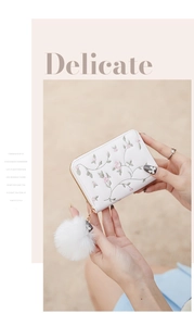 Dettaglio del portamonete in peluche bianco con ricamo floreale e ciondolo pompon soffice