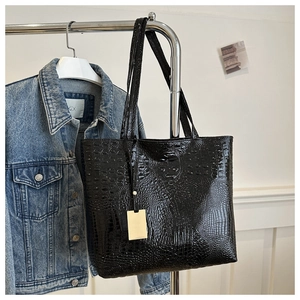 Detail of black faux crocodile texture and gold rectangular tag on the tote bag