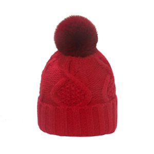 Close-up of red knit beanie with thick cable stitch and fluffy faux fur pompom detail