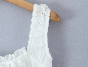 Detail of white cotton dress showing intricate lace embroidery and ruffled strap design