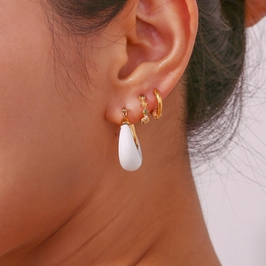 Close-up of white teardrop hoop earrings and gold ear cuffs worn by a model