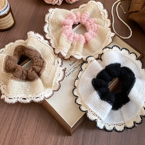Detailed knit lace hair scrunchies set in pink, beige and black on a wooden tray