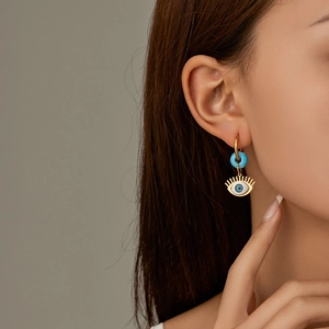 Detail view of gold stainless steel earring with blue turquoise bead and evil eye charm