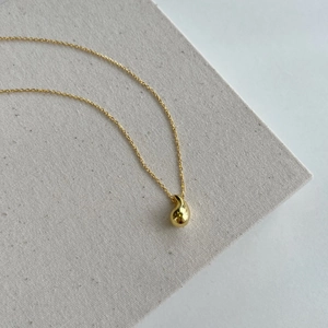 Macro shot of a golden teardrop pendant necklace on textured grey fabric background