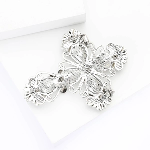 Macro detail of vintage silver cross brooch with intricate floral engravings and back pin