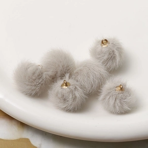 Macro shot of grey faux rabbit fur pompom charms with golden metal loops for DIY jewelry