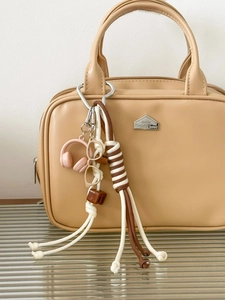 Detail of khaki handmade woven keychain with mini headphone and glasses on beige bag