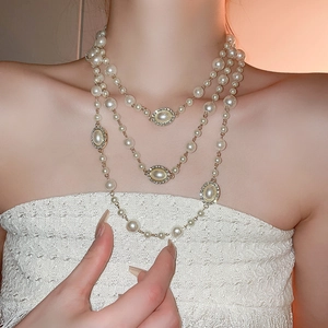 Detail of elegant three-layer pearl necklace with gold metal oval charms on model