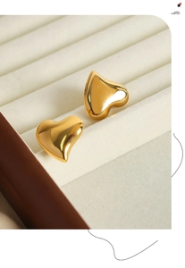 Macro shot of gold heart-shaped stud earrings with polished mirror finish in a velvet box