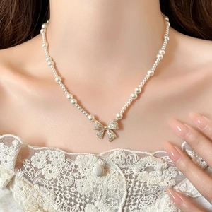 Detail of elegant pearl necklace with crystal bow pendant on lace dress