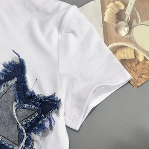 Detail of white cotton T-shirt featuring blue denim star patchwork with fringe edges