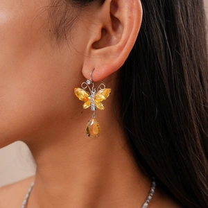 Close-up of butterfly drop earrings with yellow crystals and water drop pendant on model