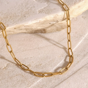 Close-up of golden paperclip chain necklace on beige stone showing polished texture