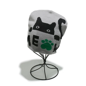 Detail showing the gray knit beanie with black cat jacquard and green paw prints