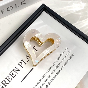 Detailed view of pearlescent white heart-shaped acetic acid hair claw with gold metal spring