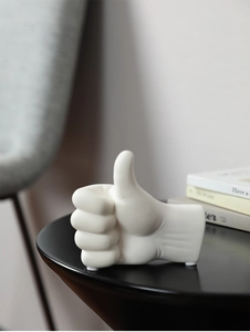 Detail view of white ceramic thumbs-up gesture sculpture on a modern black metal table