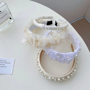 Close-up of elegant lace headband with pearls and bow details on white background