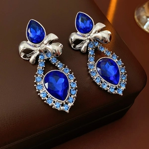 Close-up of vintage silver bow earrings with drop-shaped blue crystals on leather case