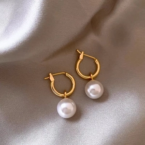 Detailed close-up of golden hoop earrings with round white pearls on silk satin