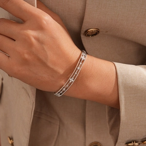 Detail of silver triple-row zircon bangle on a model's wrist with beige blazer background