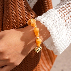 Gros plan d'un bracelet en perles de résine ambre avec détails dorés au poignet du mannequin