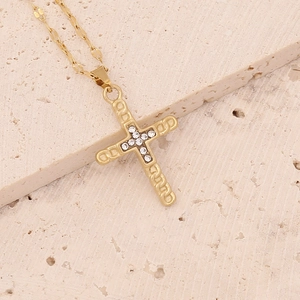 Macro detail of gold cross pendant with crystal inlay on beige textured stone surface