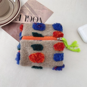 Flat lay of a plush beige cosmetic bag with colorful pom-poms next to a Vogue magazine