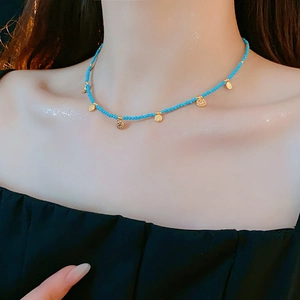 Gros plan d'un collier de perles bleues avec pendentifs dorés porté par un mannequin