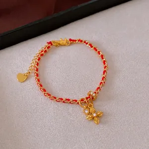Gold-plated red rope bracelet with heart and zircon cross charms on a textured background
