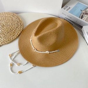 Close-up of straw sun hat featuring white shell beaded chin strap and woven texture