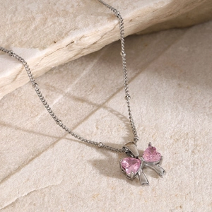 Close-up of silver beaded chain with pink heart zircon bow pendant on stone background
