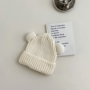 Detailed close-up of ribbed knit texture on cream baby beanie with cute double pom-poms