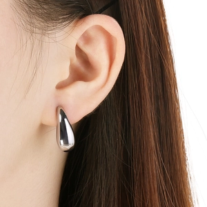 Close-up of polished silver teardrop stud earrings worn on a model with white background