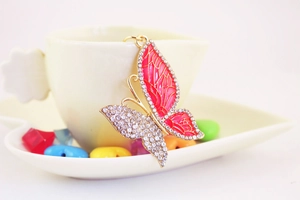 Pink butterfly keychain with gold plating and sparkling crystals on a white teacup backdrop