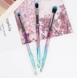 Macro detail of three eyeshadow brushes with crystal handles and blue gradient bristles