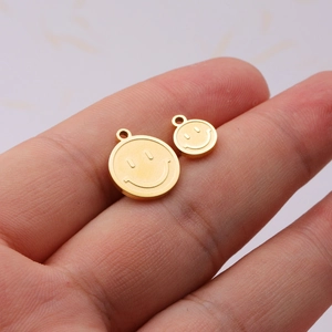 Twee gouden smiley-hangers in verschillende maten getoond op vingertoppen voor schaal