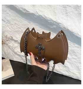Close-up of brown gothic bat bag with cross detail and chain strap on a textured wall