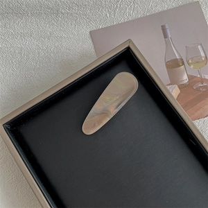Detail shot of vintage beige marble pattern hair clip on a brushed black display tray