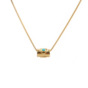 Detail view of a gold necklace featuring a cylindrical pendant with turquoise stone inlay