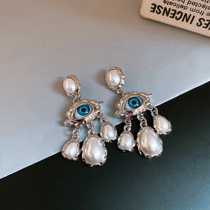 Detailed close-up of retro silver eye earrings with three dangling white pearls