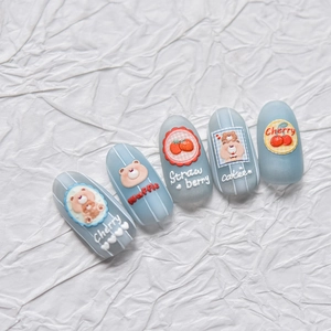 Detail of matte blue press-on nails with embossed 3D bear and fruit nail art designs