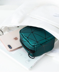 Detail of dark green geometric puzzle cosmetic bag with circular zipper pull in a tote bag