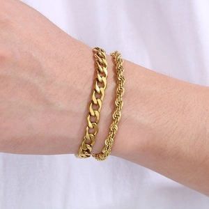 Dettaglio di bracciali a maglia cubana e a fune dorati sovrapposti sul polso maschile