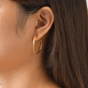 Side view of model wearing matte golden twisted C-shaped hoop earrings with a modern design