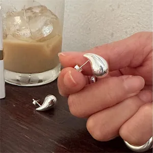 Detail of silver teardrop stud earrings on a wooden table with lifestyle coffee props
